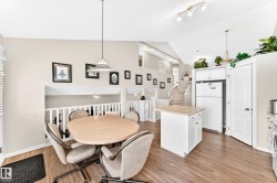 Dining area featuring wood-finish flooring, a white spindle railing, and a vaulted ceiling - 