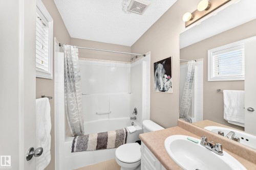 Full bathroom featuring a white tub and shower combination with a single lever faucet, a window with horizontal blinds, and a vanity with an integrated sink and mirror - 3226 30 Avenue Nw, Edmonton, AB - Indoor Photo Showing Bathroom