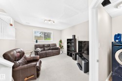 Lower level living area featuring a window, light-colored carpeting, recessed lighting, and a partial view of a laundry area with stacked appliances - 