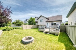 Expansive backyard featuring a stone-ringed fire pit, a wooden deck with railing, and perimeter fencing - 