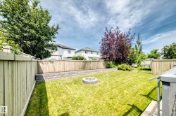Expansive backyard featuring a manicured lawn, stone fire pit, and tiered retaining wall - 
