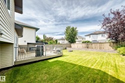 Expansive backyard featuring a green lawn, a raised wooden deck with metal railings, and a wood fence - 