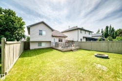Expansive backyard featuring a manicured lawn, a built-in stone fire pit, and a spacious wooden deck - 