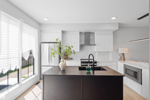 Modern kitchen featuring a large black island with an integrated sink and matte black faucet, stainless steel appliances, white cabinetry, and light wood-finish flooring - 8047 227 Street Nw, Edmonton, AB - Indoor Photo Showing Kitchen With Upgraded Kitchen