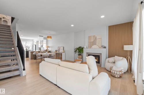 Open-concept living area featuring light wood-finish flooring, recessed lighting, and a fireplace with a stone surround - 8047 227 Street Nw, Edmonton, AB - Indoor Photo Showing Living Room With Fireplace