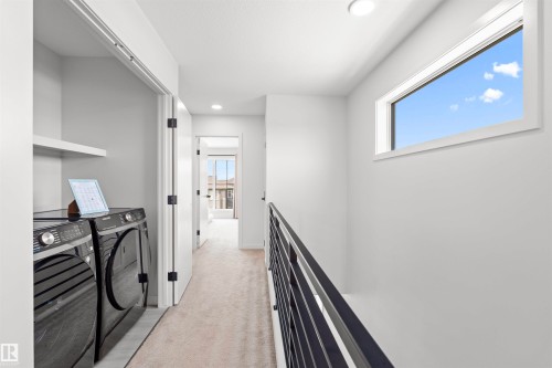Upper-level hallway featuring a laundry closet with built-in shelving, a horizontal window, recessed lighting, and a contemporary black metal stair railing - 8047 227 Street Nw, Edmonton, AB - Indoor Photo Showing Other Room