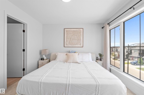 Carpeted bedroom featuring an expansive window with black grid panes, light gray wall paint, a built-in light fixture, and a solid gray door with black hardware - 8047 227 Street Nw, Edmonton, AB - Indoor Photo Showing Bedroom