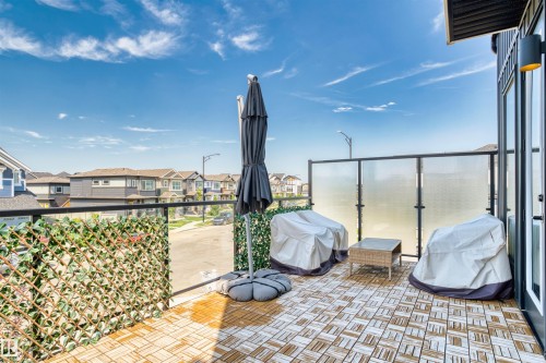 Spacious outdoor balcony featuring patterned tile flooring, a glass railing with a privacy screen, and a modern exterior wall sconce - 8047 227 Street Nw, Edmonton, AB - Outdoor With Balcony