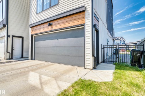 Modern garage exterior featuring a grey sectional door, accent wood-finish paneling, and black trim - 8047 227 Street Nw, Edmonton, AB - Outdoor
