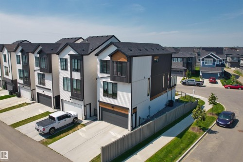 Modern townhome exterior featuring white siding, dark accent panels, and a black shingle roof - 8047 227 Street Nw, Edmonton, AB - Outdoor