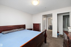 Carpeted room featuring a white ceiling and walls, with an entrance to a bathroom area showcasing a vanity and mirror, and a separate opening revealing a shower stall - 