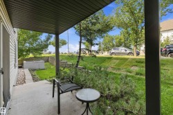 Covered concrete patio featuring a concrete retaining wall, mature trees, and landscaping - 