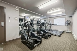 Dedicated fitness area featuring multiple cardio machines, full-wall mirror, window with horizontal blinds, and overhead fluorescent lighting - 