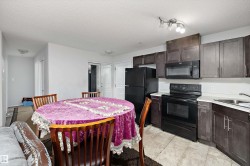 Open-concept kitchen featuring dark wood-finish cabinetry, black appliances, light countertops, and tile flooring - 