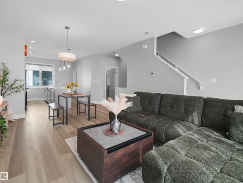 Open-concept living area featuring wood-finish flooring, recessed lighting, and a contemporary pendant fixture - #81 6905 25 Av Sw, Edmonton, AB - Indoor Photo Showing Living Room