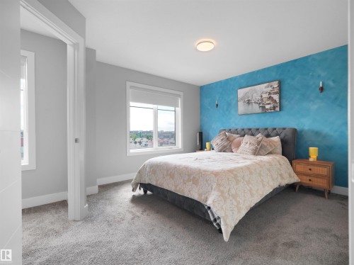 Bedroom featuring a textured accent wall, plush carpeting, and two large windows - #81 6905 25 Av Sw, Edmonton, AB - Indoor Photo Showing Bedroom