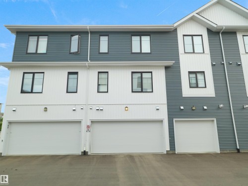 Contemporary multi-story exterior featuring white and blue siding, black-framed windows, and multiple garage doors - #81 6905 25 Av Sw, Edmonton, AB - Outdoor