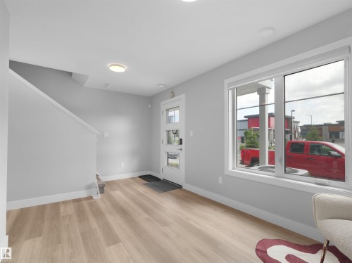 Open entryway featuring wood-finish flooring, a contemporary front door with horizontal glass panels, and a large window with white trim - #81 6905 25 Av Sw, Edmonton, AB - Indoor Photo Showing Other Room