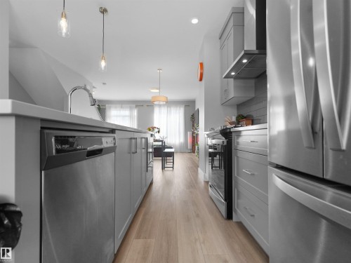 Modern kitchen featuring light gray cabinetry, stainless steel appliances, a pull-down faucet, and wood-finish flooring - #81 6905 25 Av Sw, Edmonton, AB - Indoor Photo Showing Kitchen