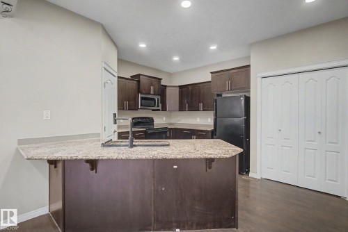 Kitchen featuring dark wood cabinetry, light speckled countertops, and wood-finish flooring - 315 Watt Boulevard Sw, Edmonton, AB 