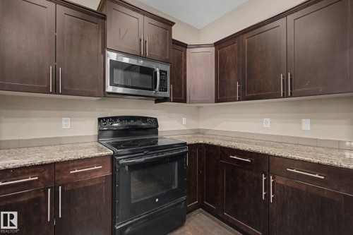 Kitchen featuring dark wood-finish cabinetry, light-toned countertops, and a full-size black electric range with an overhead stainless steel microwave - 315 Watt Boulevard Sw, Edmonton, AB 
