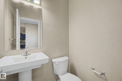 Pedestal sink with chrome faucet, wall-mounted mirror, white toilet, and neutral wall paint - 