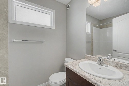 Bathroom featuring a dark wood-finish vanity with an undermount sink, a light speckled countertop, and a shower with tiled walls - 315 Watt Boulevard Sw, Edmonton, AB 