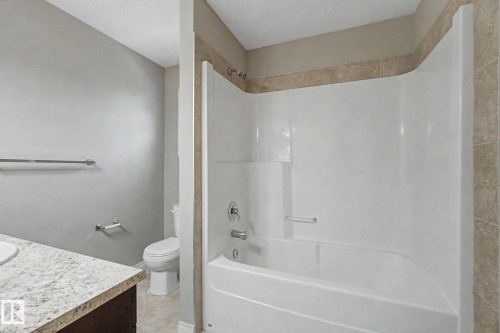 Full bath featuring a white tub/shower combination with integrated shelving, chrome fixtures, and tan tile surround - 315 Watt Boulevard Sw, Edmonton, AB 