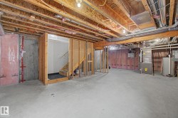 Unfinished lower level offering concrete flooring, exposed ceiling joists, framed stairwell, and visible utility systems - 