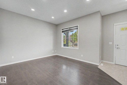 Open-concept living space with dark wood-finish flooring, recessed lighting, a large window with roller shades, and light gray wall tones - 315 Watt Boulevard Sw, Edmonton, AB 