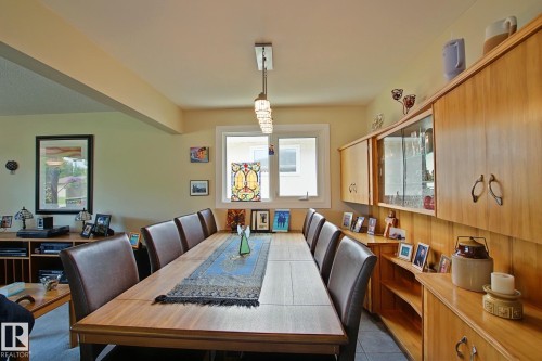 Dining area featuring a long wood-finish table with seating, built-in blonde wood cabinetry with glass-front display sections, and a horizontal window providing natural light - 3536 104 Street Nw, Edmonton, AB - Indoor Photo Showing Dining Room