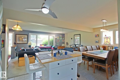 Open-concept living area featuring a central island with built-in storage, a dining space with a multi-light chandelier, and an expansive window in the living room - 3536 104 Street Nw, Edmonton, AB - Indoor Photo Showing Dining Room