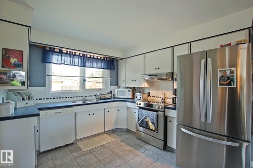 Kitchen featuring white cabinetry with black hardware, dark countertops, and a white tile backsplash - 3536 104 Street Nw, Edmonton, AB - Indoor Photo Showing Kitchen With Double Sink