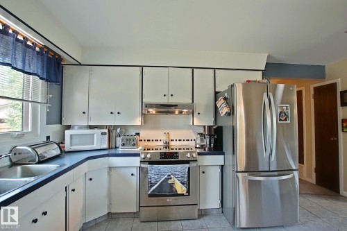 Kitchen featuring white cabinetry with dark hardware, a stainless steel refrigerator, a stainless steel range with overhead microwave, a double basin sink, and tile flooring - 3536 104 Street Nw, Edmonton, AB - Indoor Photo Showing Kitchen