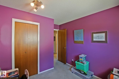 Interior room featuring a textured ceiling, a flush-mount light fixture with three spotlights, a bi-fold closet door with wood-finish panels, and light-colored carpeting - 3536 104 Street Nw, Edmonton, AB - Indoor