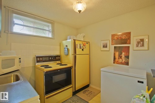Compact kitchen area featuring a window with horizontal blinds, a built-in electric range, and a single-basin sink with an integrated countertop - 3536 104 Street Nw, Edmonton, AB - Indoor