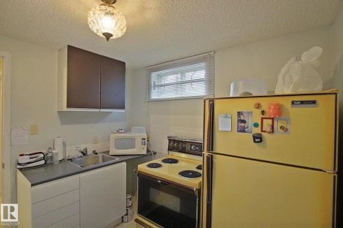 Compact kitchen area featuring a double-basin stainless steel sink, dark countertops, and overhead brown cabinetry - 3536 104 Street Nw, Edmonton, AB - Indoor