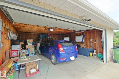 Attached garage with overhead door and automatic opener, featuring exposed wood framing, concrete flooring, and an additional side entrance - 3536 104 Street Nw, Edmonton, AB - Indoor Photo Showing Garage