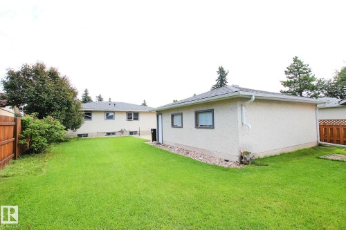 Expansive rear yard featuring a manicured lawn, a detached garage with textured stucco finish, and a wood privacy fence - 3536 104 Street Nw, Edmonton, AB - Outdoor