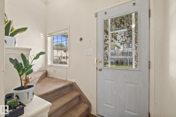 Entryway featuring a white paneled door with a decorative glass insert, a staircase with carpeted treads, and a window with blinds - 
