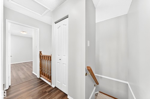 Upper-level hallway featuring wood-finish flooring, light gray walls, white trim, and a white bi-fold closet door - 22 Woodvale Village Nw, Edmonton, AB - Indoor Photo Showing Other Room