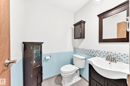 Bathroom featuring a vanity with an integrated sink, a dark wood-finish framed mirror, and a mosaic tile accent band - 22 Woodvale Village Nw, Edmonton, AB - Indoor Photo Showing Bathroom