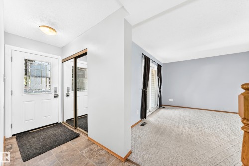 Entryway featuring a white front door with decorative glass, adjacent mirrored closet doors, and tile flooring - 22 Woodvale Village Nw, Edmonton, AB - Indoor Photo Showing Other Room