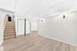 Expansive lower-level room featuring wood-finish flooring, white panel walls, and a drop ceiling with integrated lighting - 