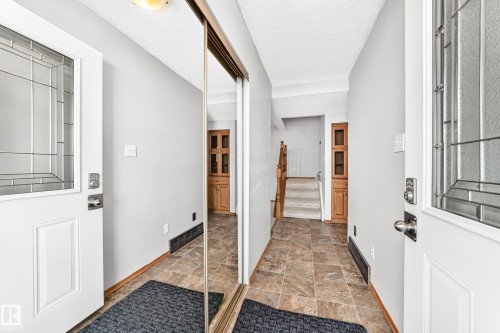 Entryway featuring two white doors with decorative glass inserts, an overhead light fixture, wood-finish baseboards, and a mirrored closet door - 22 Woodvale Village Nw, Edmonton, AB - Indoor Photo Showing Other Room