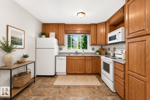 Kitchen featuring wood-finish cabinetry, patterned tile backsplash, and a window above the sink - 22 Woodvale Village Nw, Edmonton, AB - Indoor Photo Showing Kitchen With Double Sink