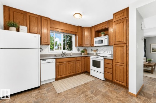 Kitchen featuring wood cabinetry, white appliances, a patterned backsplash, and a window above the sink - 22 Woodvale Village Nw, Edmonton, AB - Indoor Photo Showing Kitchen With Double Sink