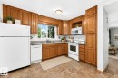 Kitchen featuring wood cabinetry, white appliances, a patterned backsplash, and a window above the sink - 22 Woodvale Village Nw, Edmonton, AB  - Indoor Photo Showing Kitchen With Double Sink 