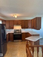 Kitchen featuring wood cabinetry, light-toned countertops, a stainless steel electric range, and a black stainless steel refrigerator - 