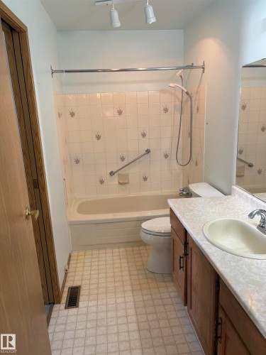 Bathroom featuring a white bathtub, decorative tile surround, track lighting, vanity with integrated sink, and patterned flooring - 17520 Callingwood Road Nw, Edmonton, AB - Indoor Photo Showing Bathroom